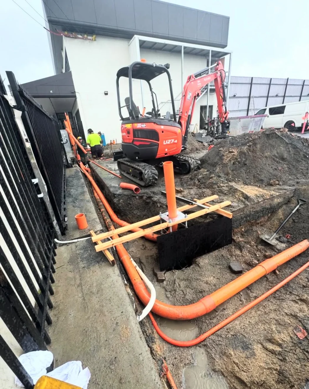 Excavator beside a trench with orange underground conduits at a civil works site